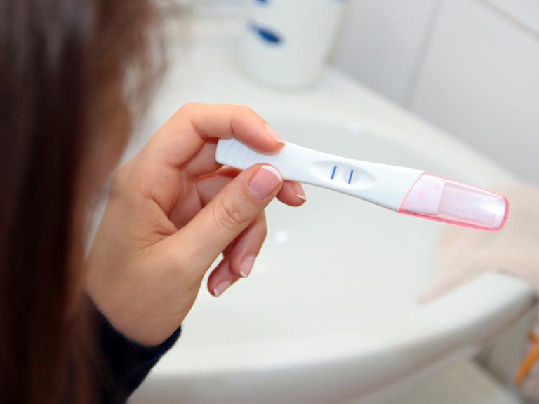 Eine Frau blickt auf einen positiven Schwangerschaftstest.