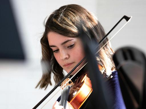 Eine Jugendliche mit schulterlangen braunen Haaren spielt konzentriert Geige.