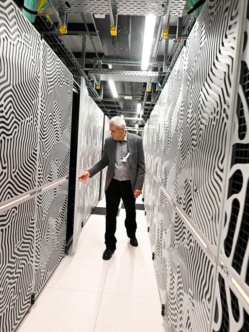 Ein Mitarbeiter steht in einem Flur zwischen den Servern des Supercomputers Jupiter.