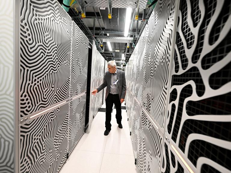 Ein Mitarbeiter steht in einem Flur zwischen den Servern des Supercomputers Jupiter.