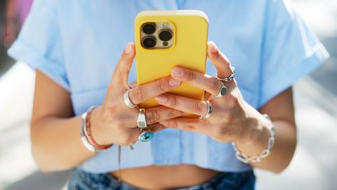 Nahaufnahme einer Frau, die ihr knallgelbes Smartphone in den Händen hält und tippt