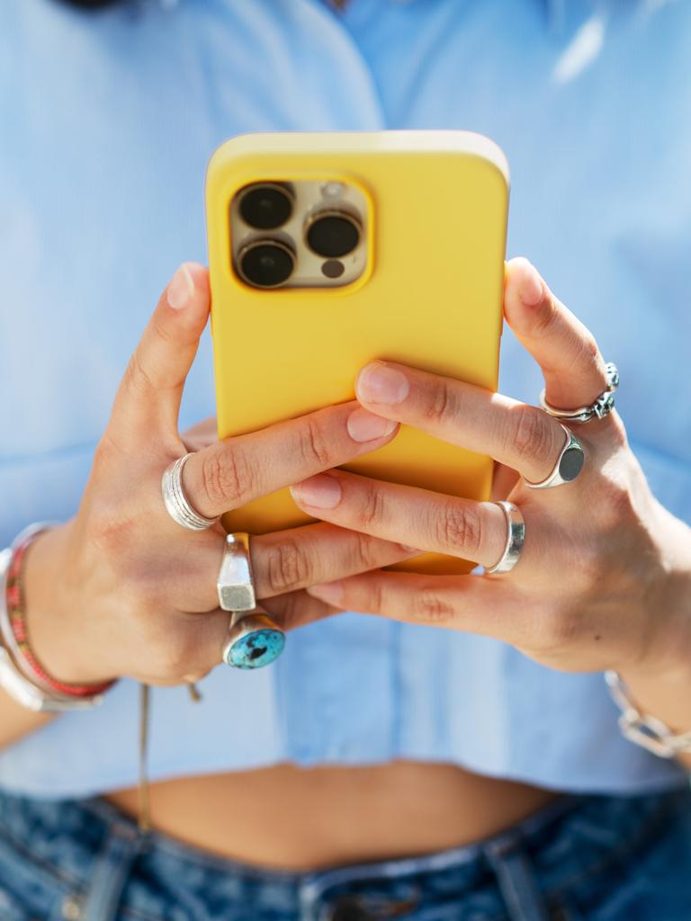 Nahaufnahme einer Frau, die ihr knallgelbes Smartphone in den Händen hält und tippt