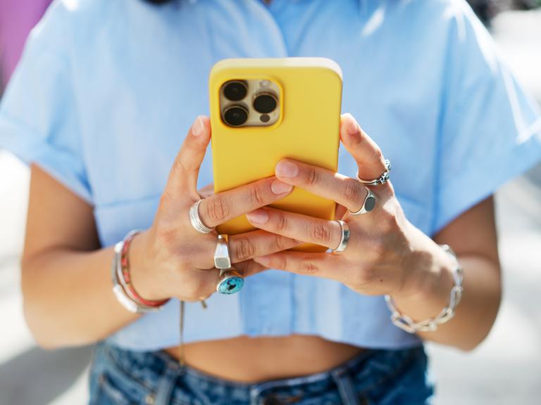 Nahaufnahme einer Frau, die ihr knallgelbes Smartphone in den Händen hält und tippt