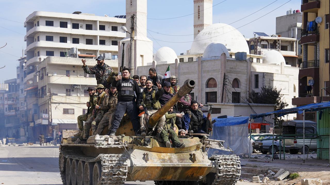 Ein Dutzend syrische Sicherheitsleute auf einem Panzer, im Hintergrund eine Moschee