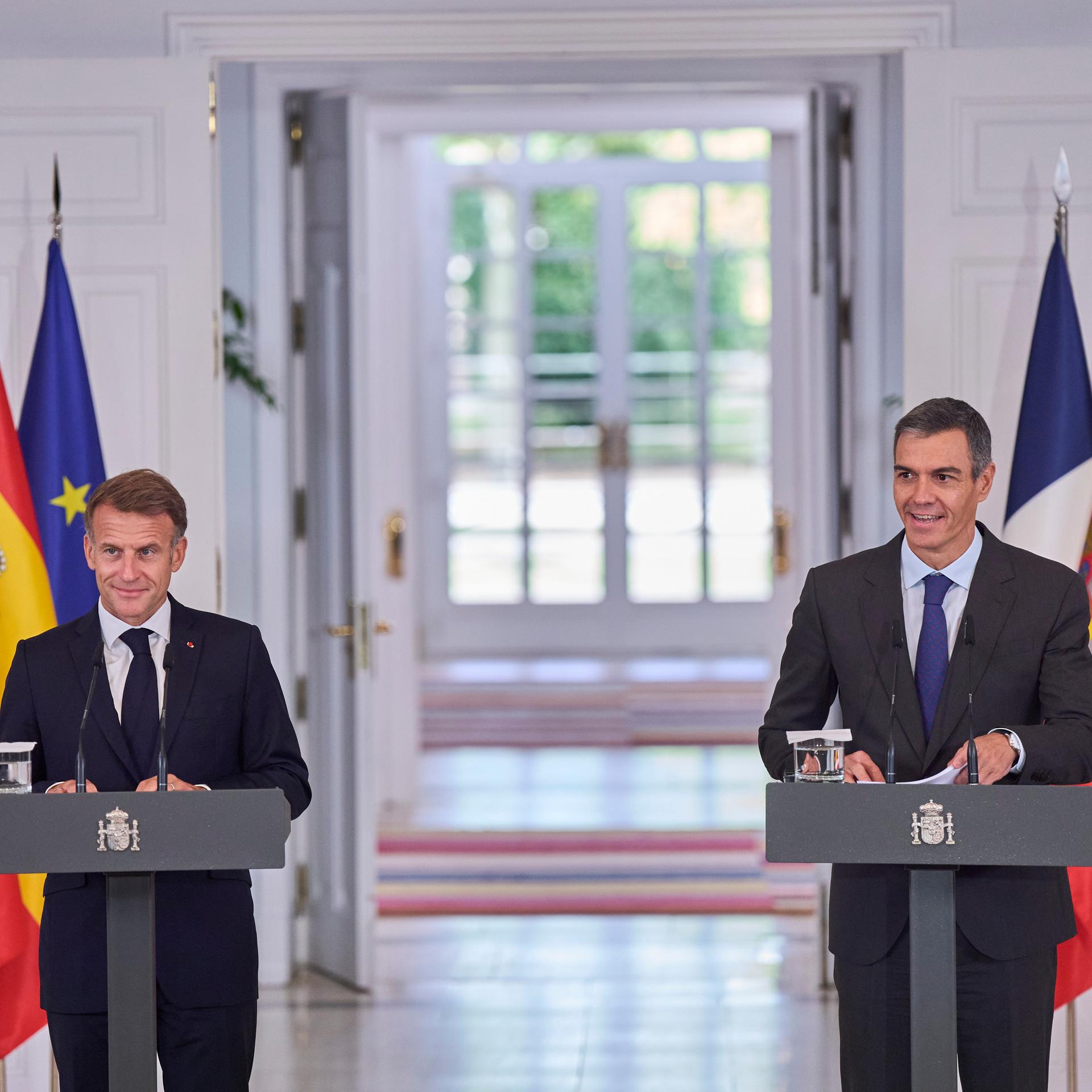 Der spanische Ministerpräsident Pedro Sánchez und der französische Präsident Emmanuel Macron bei einem Treffen im Moncloa-Palast in Madrid. Im Hintergrund sind Flaggen drapiert. 