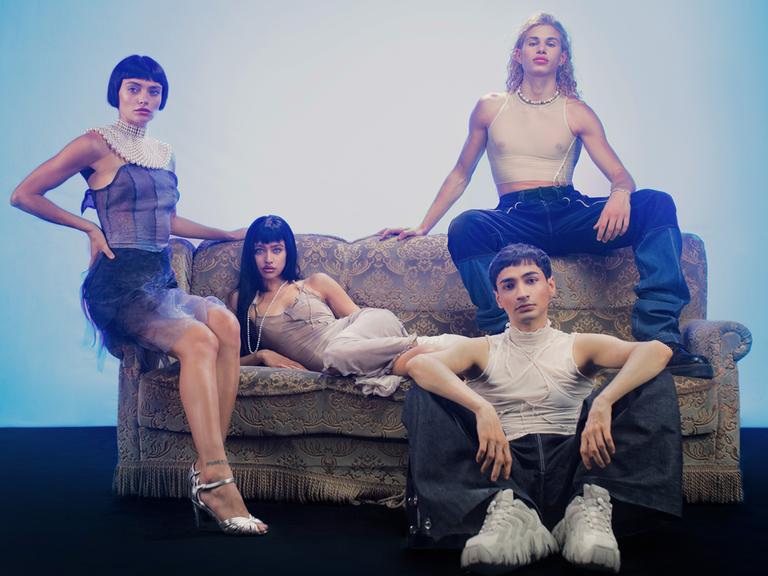 Studiofoto mit den ukrainischen und russischen Models Valeriia Karamann (links), Tanya Chudnovskaia (2. von links) Daniel Nikiforow (rechts oben) und Regisseur und Fotograf Mehran Djojan (rechts unten sitzend). Die jungen Leute sind stylisch frisiert und gekleidet.