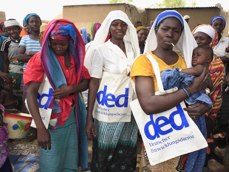 Frauen in einem Dorf der Region FadaNgourma in Burkina Faso tragen Taschen mit dem Logo des DED (Deutscher Entwicklungsdienst).