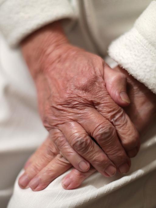 Nahaufnahme von zwei Händen eines alten Menschen, die übereinander liegen - die eine Hand scheint die andere festzuhalten.
