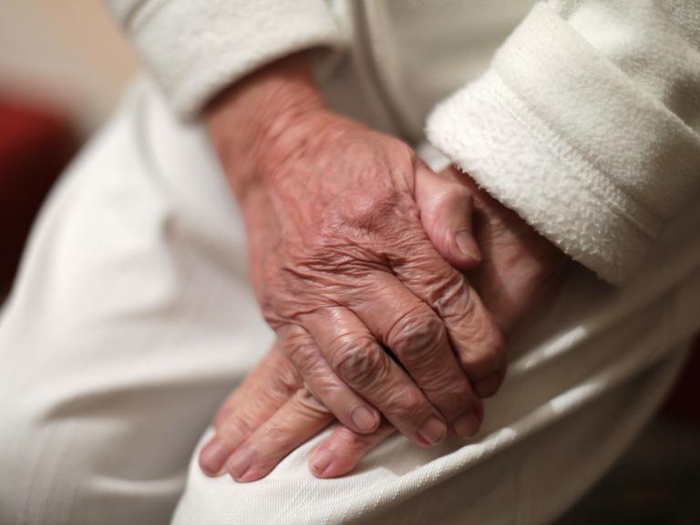 Nahaufnahme von zwei Händen eines alten Menschen, die übereinander liegen - die eine Hand scheint die andere festzuhalten.