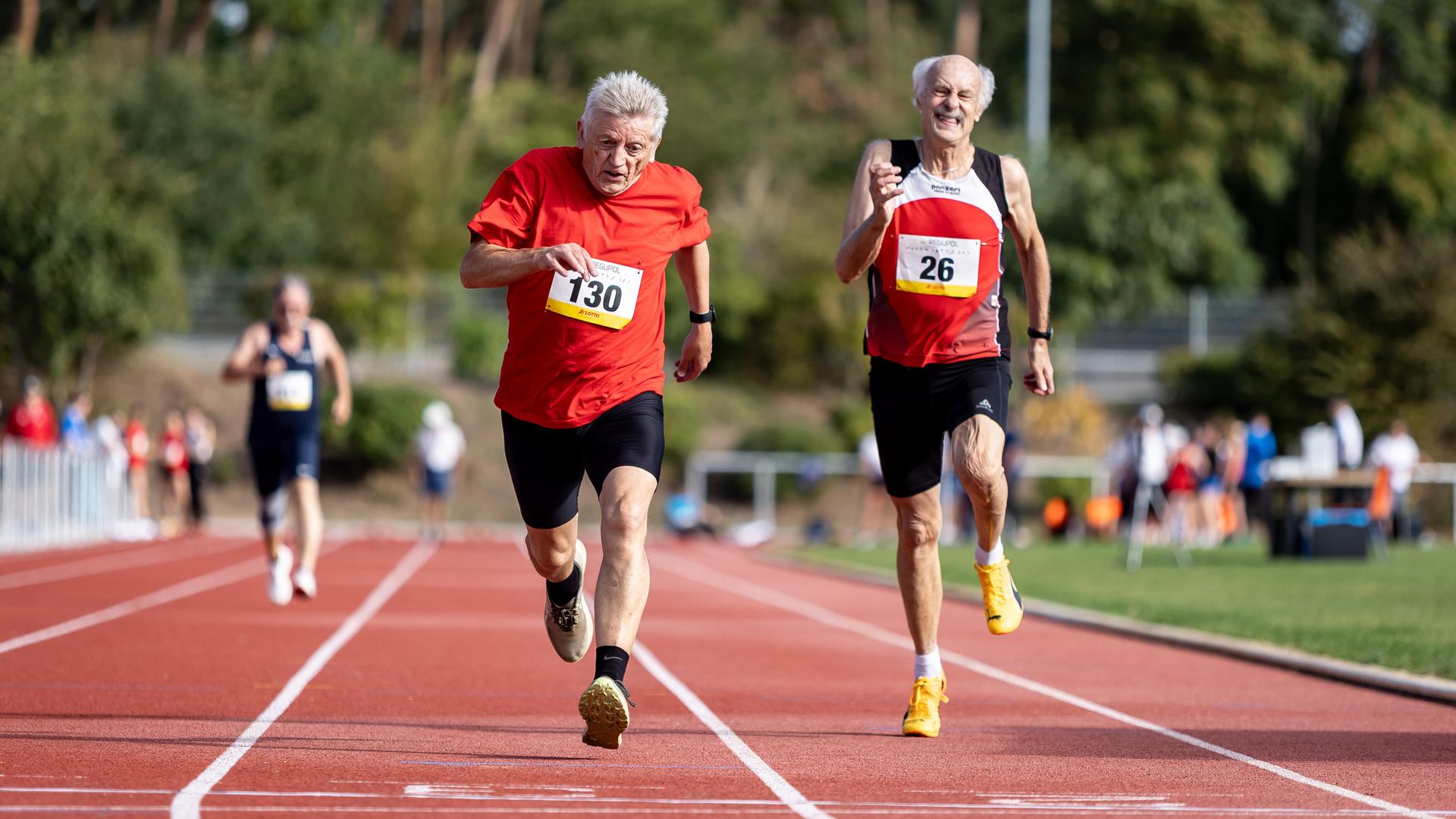 Zwei ältere Männer laufen auf einem Sportplatz um die Wette.