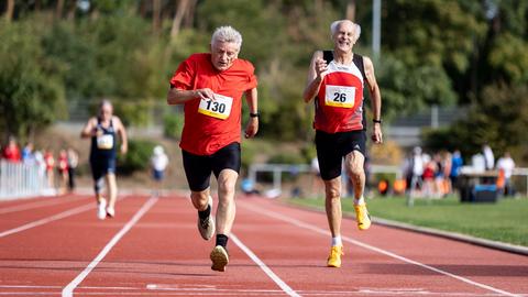 Zwei ältere Männer laufen auf einem Sportplatz um die Wette. Zwei ältere Männer laufen auf einem Sportplatz um die Wette.