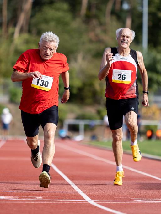 Zwei ältere Männer laufen auf einem Sportplatz um die Wette. Zwei ältere Männer laufen auf einem Sportplatz um die Wette.