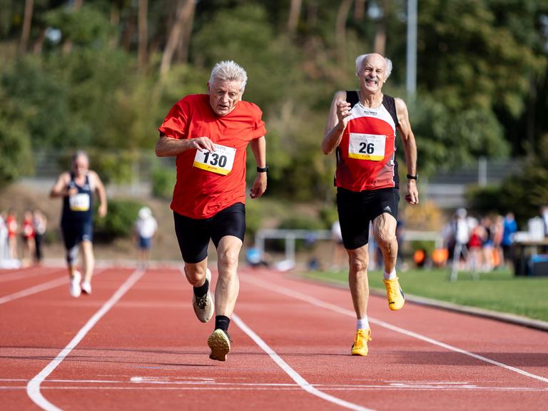 Zwei ältere Männer laufen auf einem Sportplatz um die Wette. Zwei ältere Männer laufen auf einem Sportplatz um die Wette.