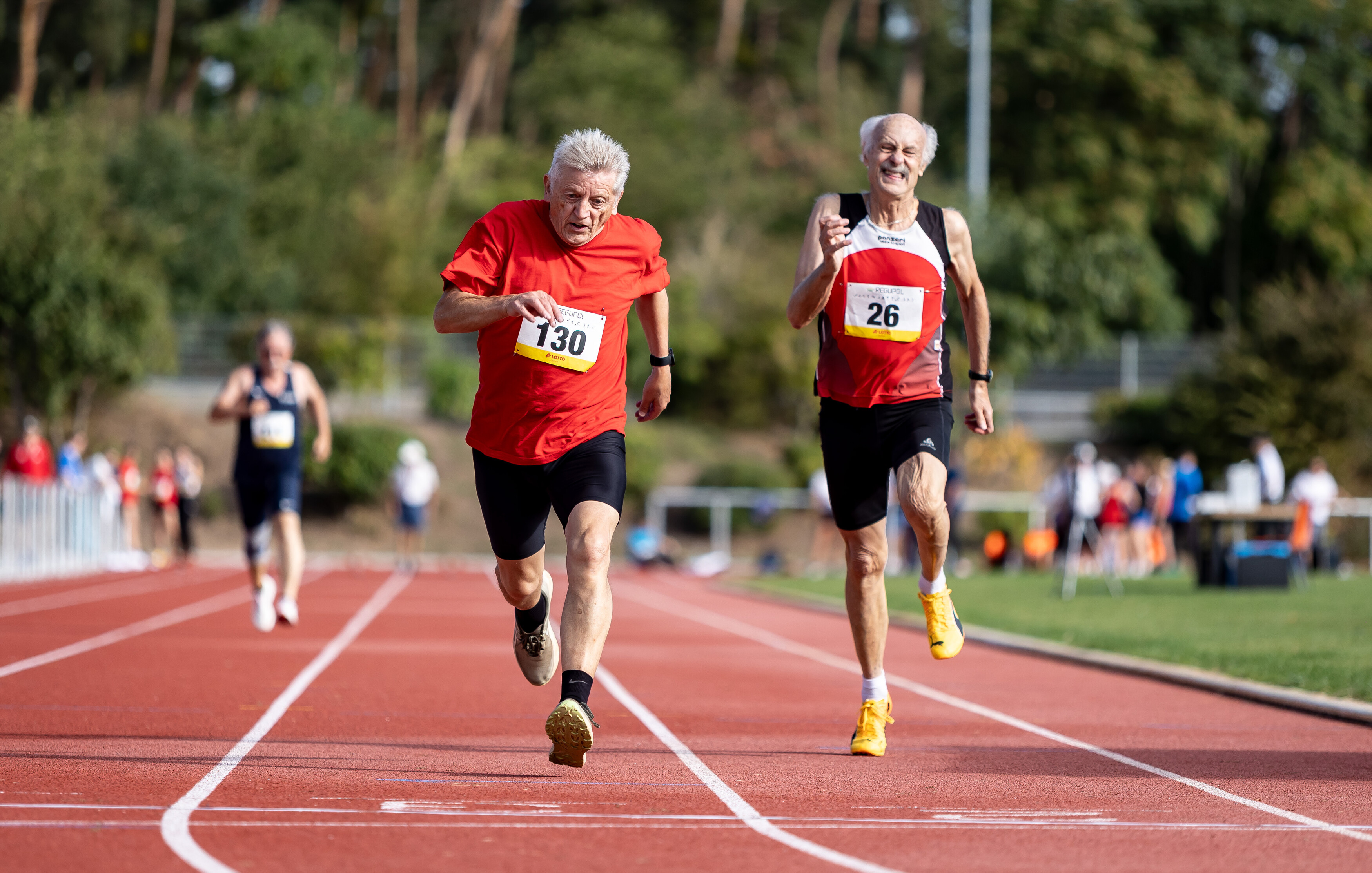 Zwei ältere Männer laufen auf einem Sportplatz um die Wette.