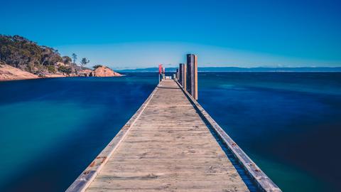 Ein lang gezogener Anlegesteg aus Holz führt unter einem knallblauen Himmel durch  tiefblaues Wasser.