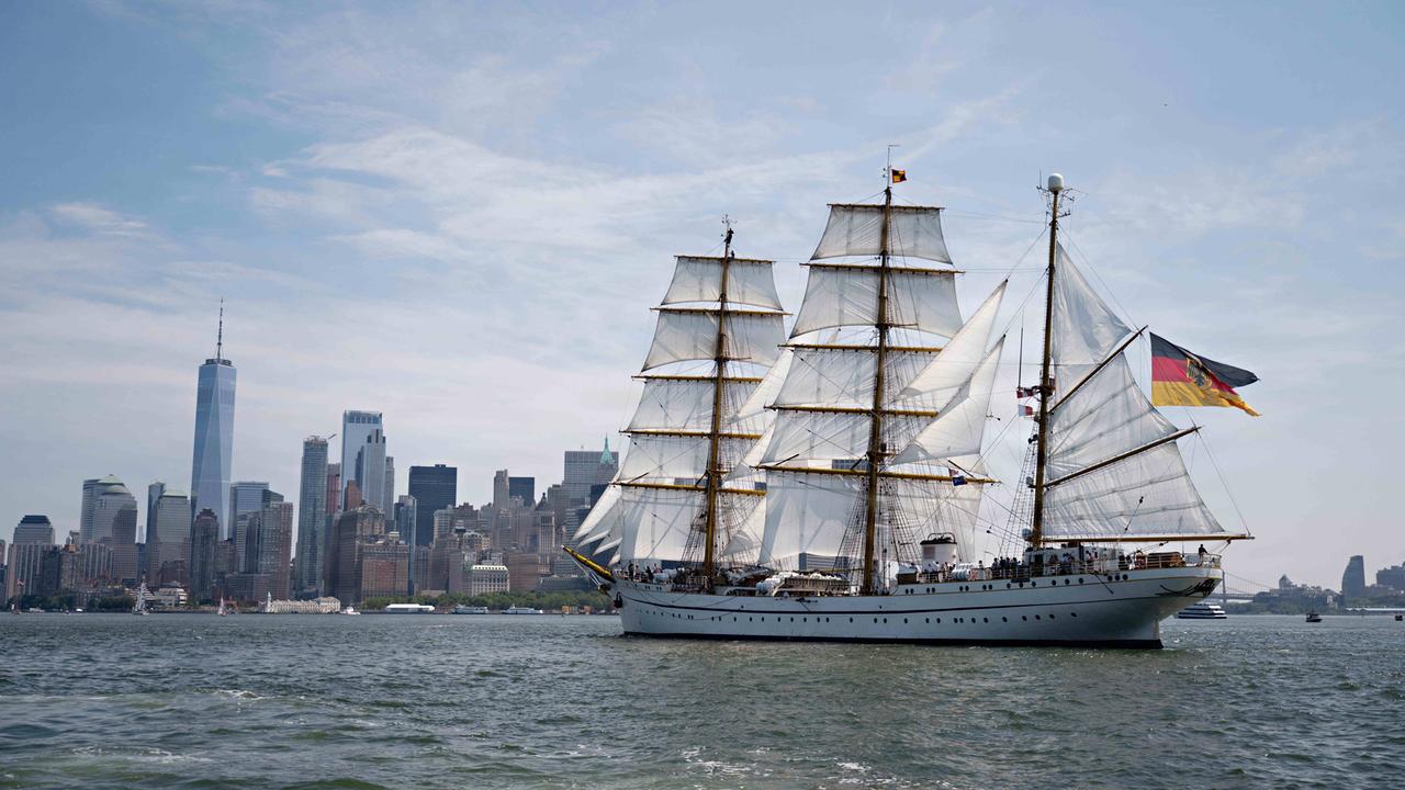 Abgebildet ist das deutsche Marineschiff „Gorch Fock“ auf dem Hudson River mit gehissten Segeln. Im Hintergrund sind die Wolkenkratzer Manhattans. 