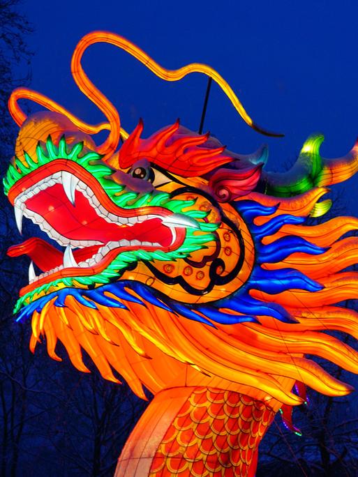 Der flammende Kopf der Skulptur eines chinesischen Drachen leuchtet in der Nacht, das Maul und die Augen weit aufgerissen.