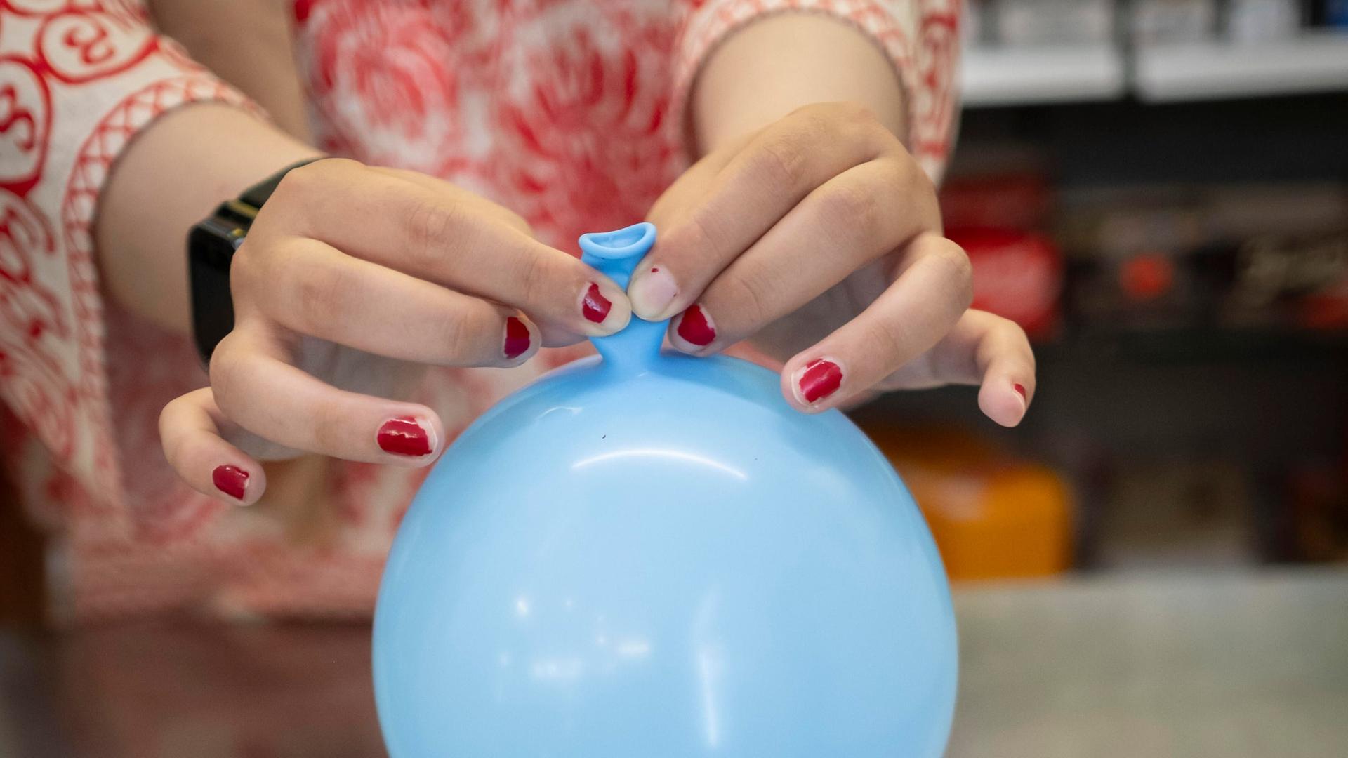 Zwei Hände halten einen blauen Ballon. Die Hände sehen jung aus. Auf den Fingernägeln blättert roter Nagellack etwas ab. 