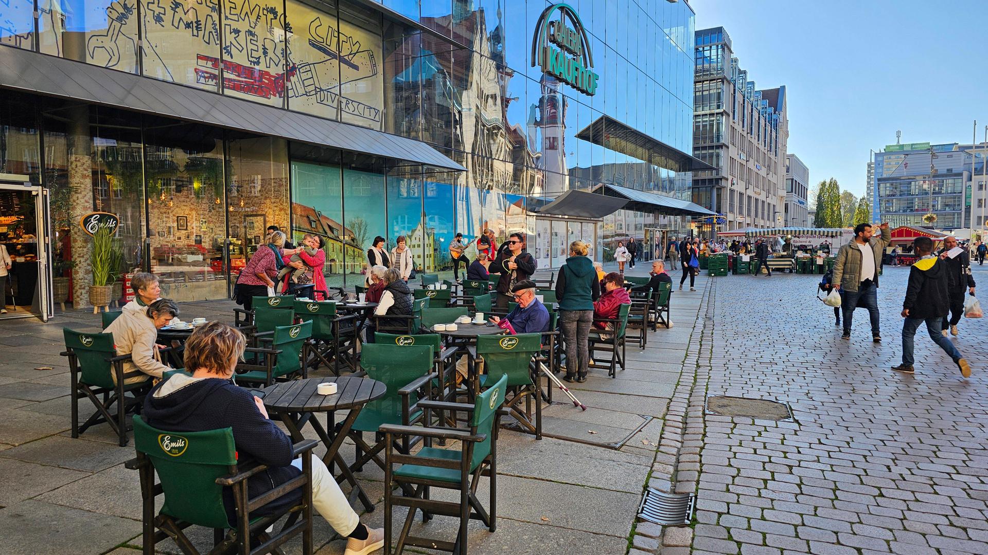 Menschen sitzen im Freien auf dem Marktplatz von Chemnitz in einem Café an Tischen.