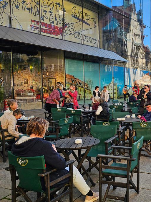 Menschen sitzen im Freien auf dem Marktplatz von Chemnitz in einem Café an Tischen.