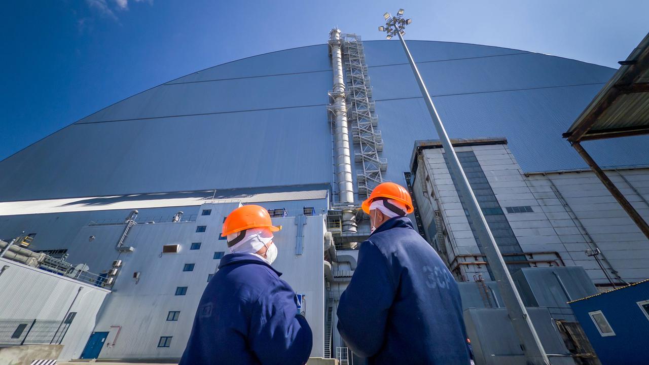 Zwei Arbeiter stehen vor der Schutzhülle am havarierten Reaktor in Tschernobyl