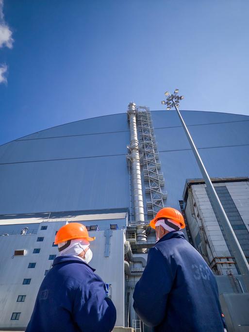 Zwei Arbeiter stehen vor der Schutzhülle am havarierten Reaktor in Tschernobyl