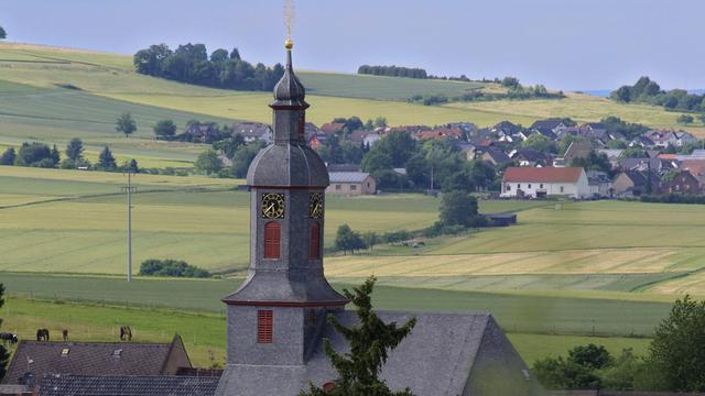 Blick auf ein Dorf mit Kirchturm inmitten von Feldern im Landkreis Limburg-Weilburg.