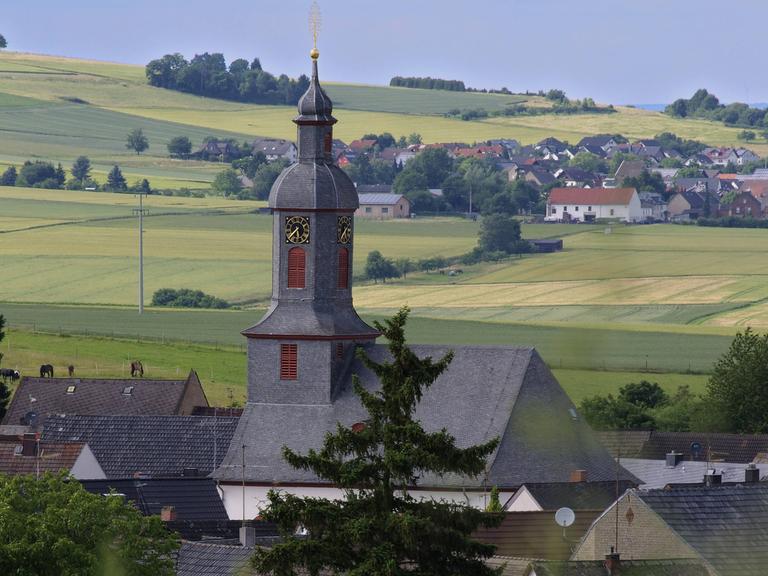 Blick auf ein Dorf mit Kirchturm inmitten von Feldern im Landkreis Limburg-Weilburg.