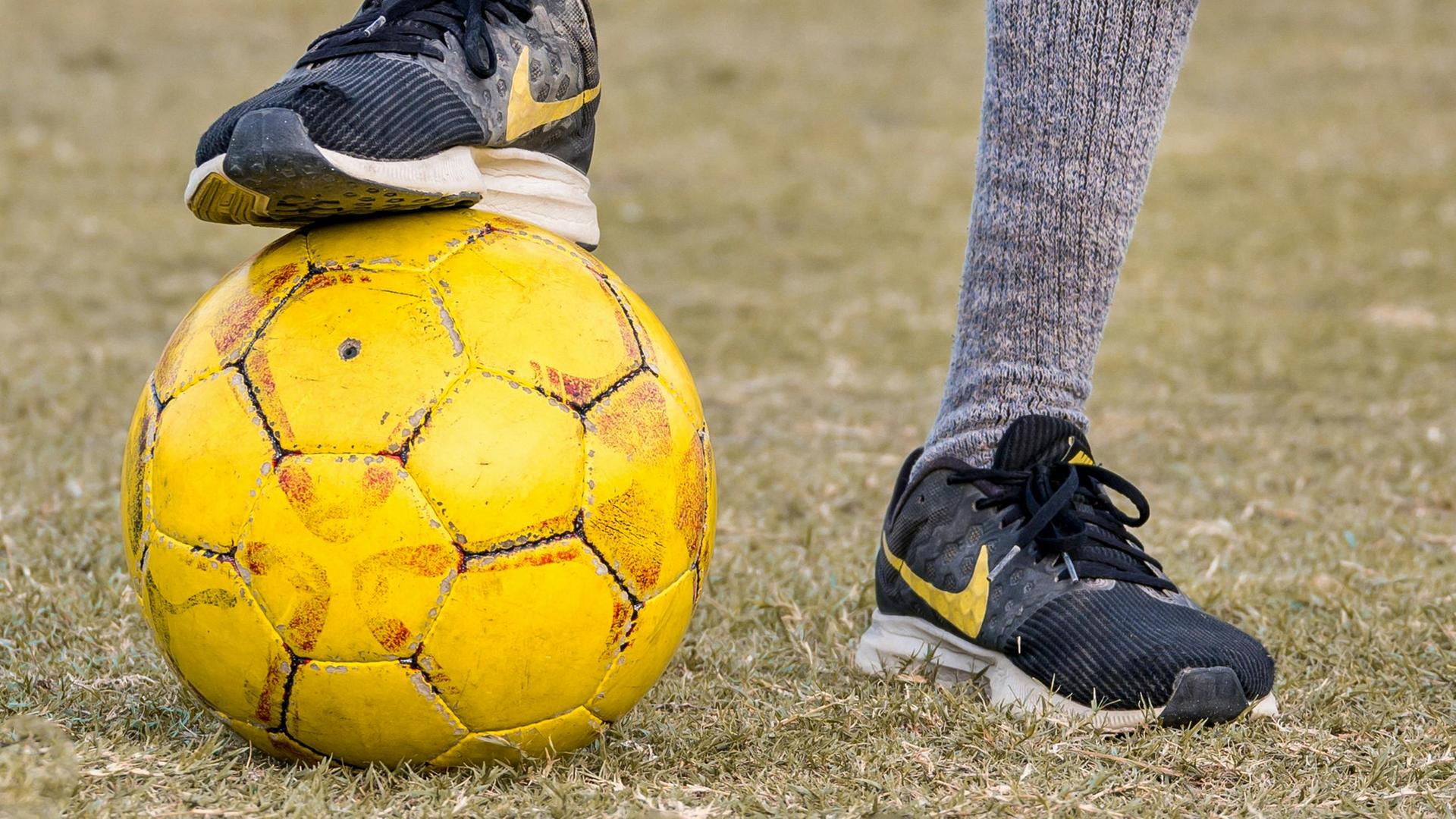 Ein Fußballer hat einen Fuß auf einen gelben Ball stellt. 