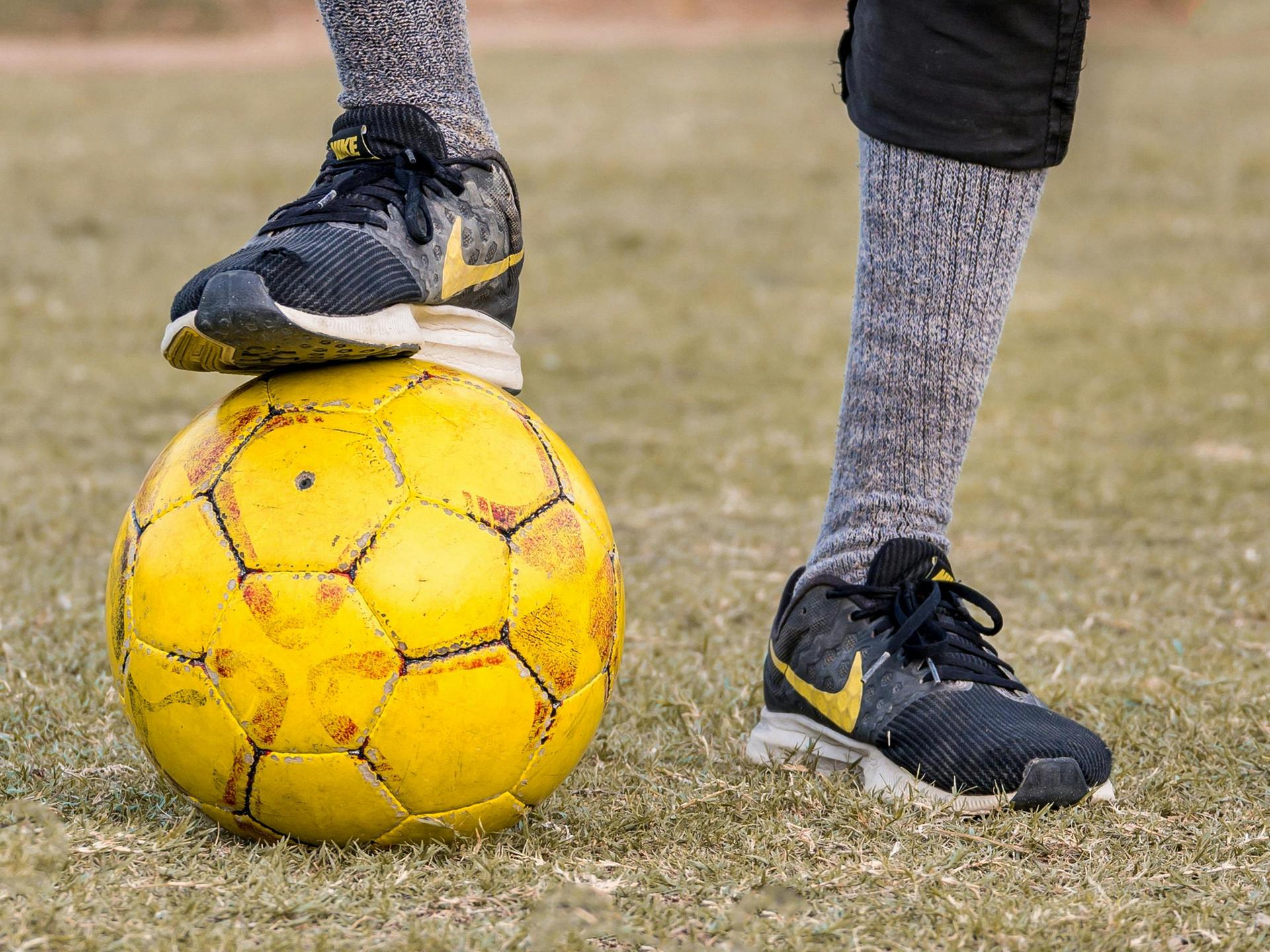 Ein Fußballer hat einen Fuß auf einen gelben Ball stellt. 
