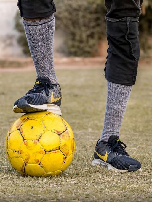 Ein Fußballer hat einen Fuß auf einen gelben Ball stellt. 