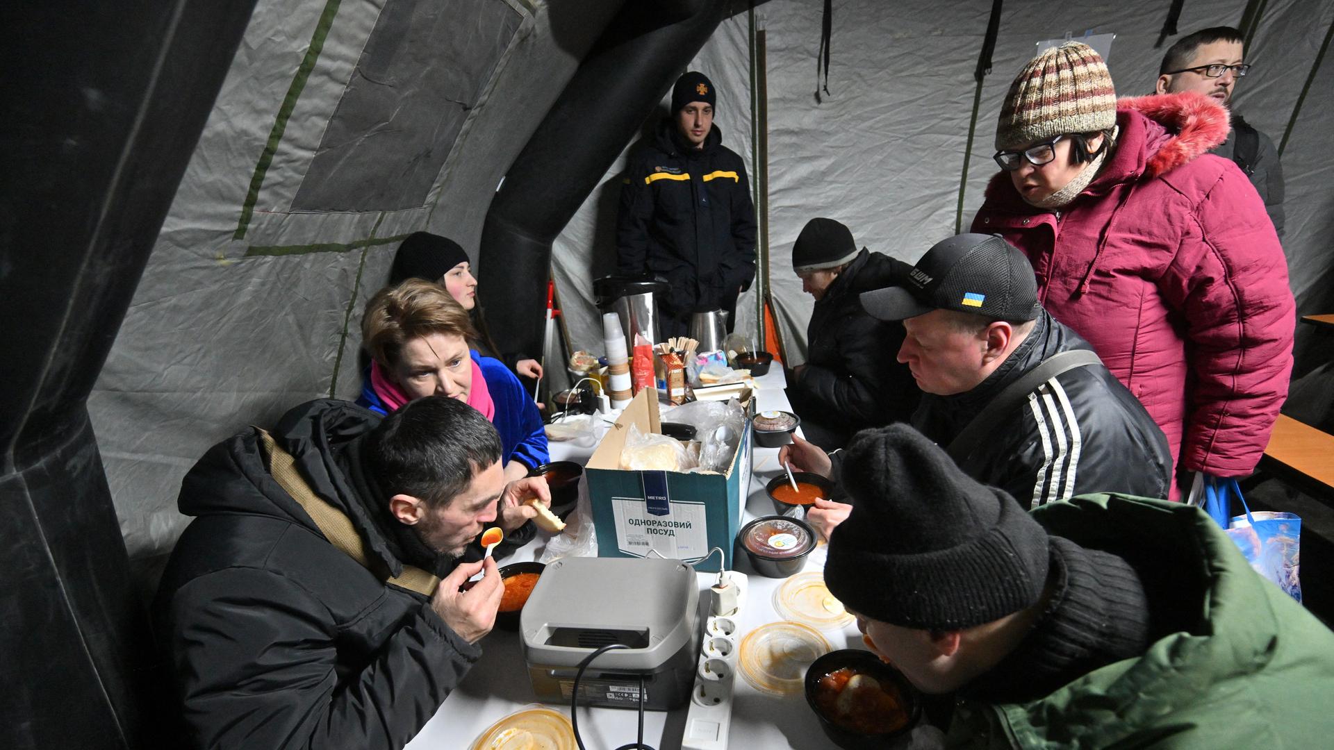Menschen sitzen in Kiew in einem Zelt und nehmen eine warme Mahlzeit zu sich.