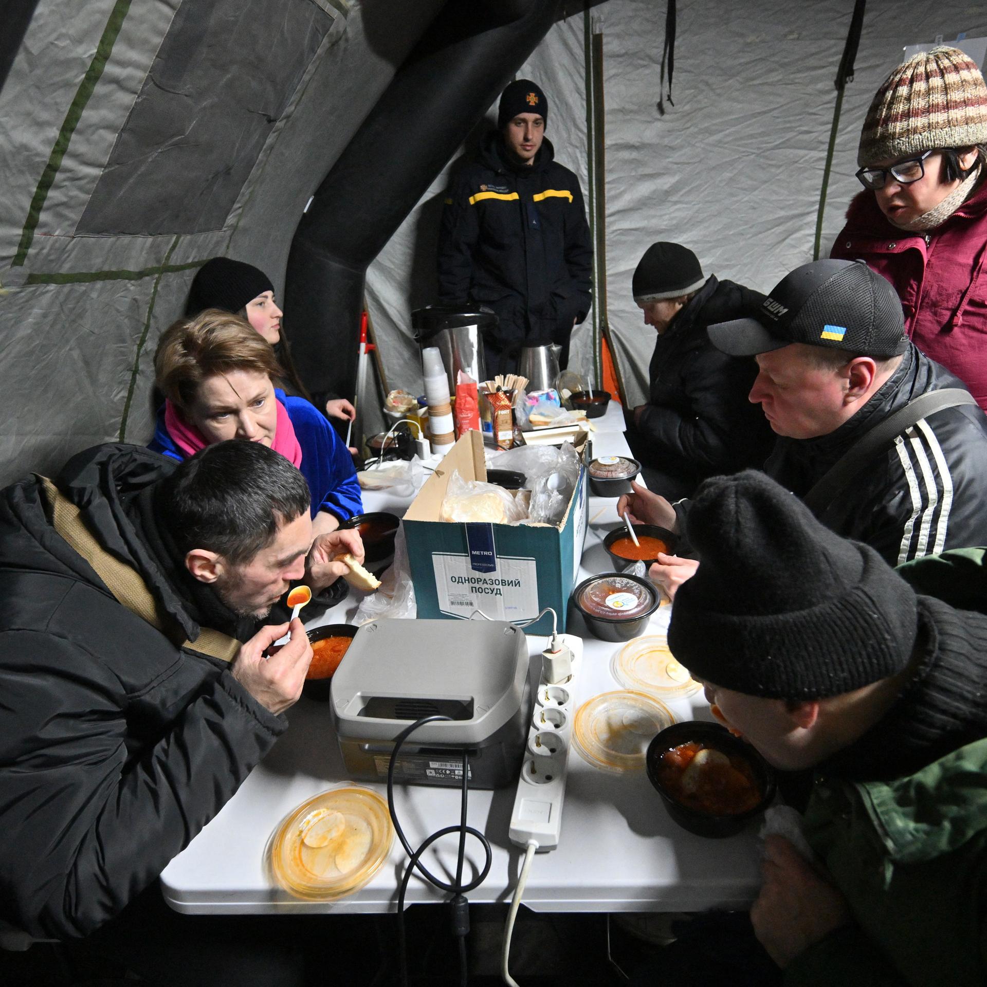 Menschen sitzen in Kiew in einem Zelt und nehmen eine warme Mahlzeit zu sich.