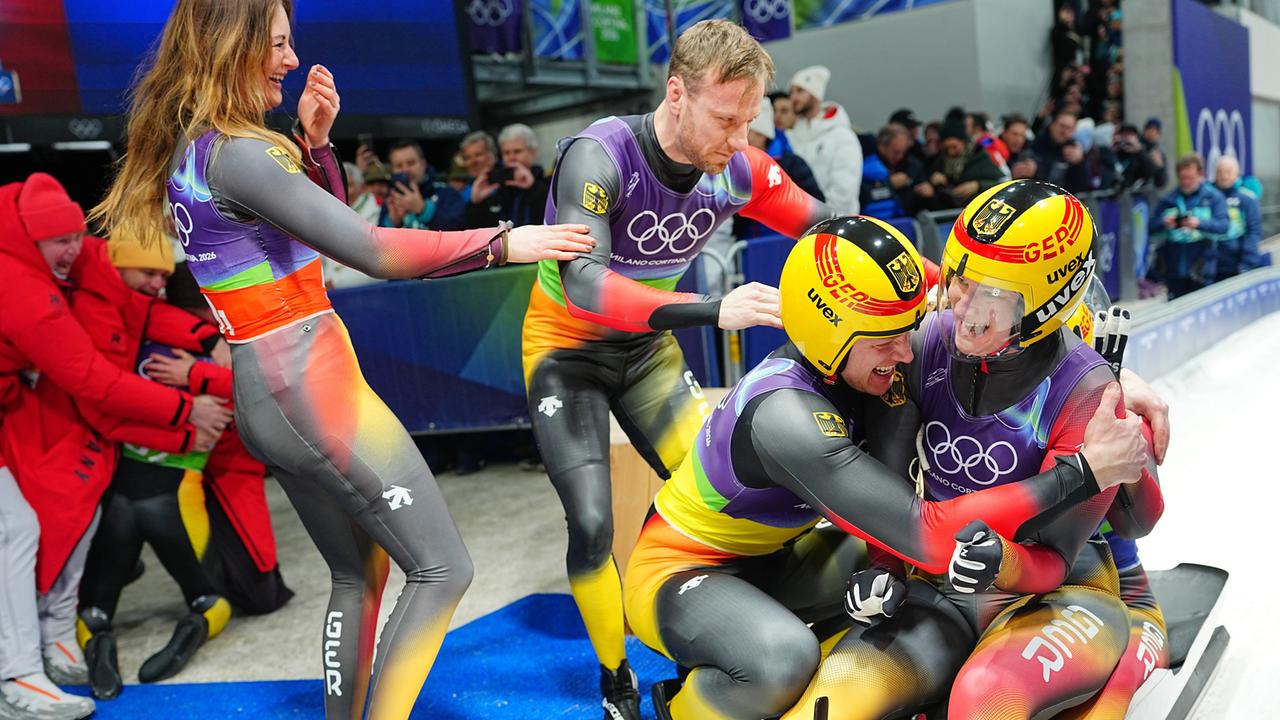 Die deutschen Rodlerinnen und Rodler umarmen sich im Ziel und jubeln.