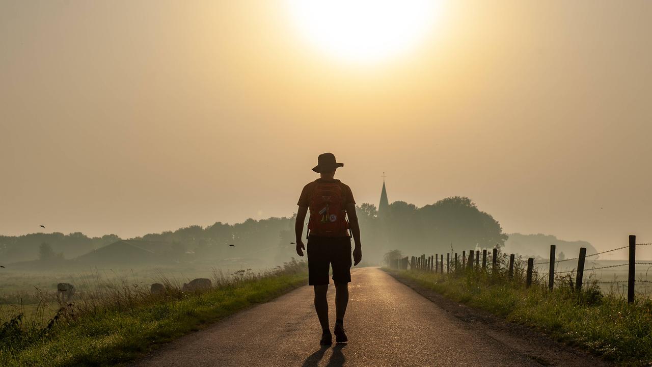 Ein Mann läuft während eines vernebelten Sonnenaufgangs auf einem Deich entlang. Das Bild symbolisiert die große Hitze, die der Klimawandel mit sich bringt.