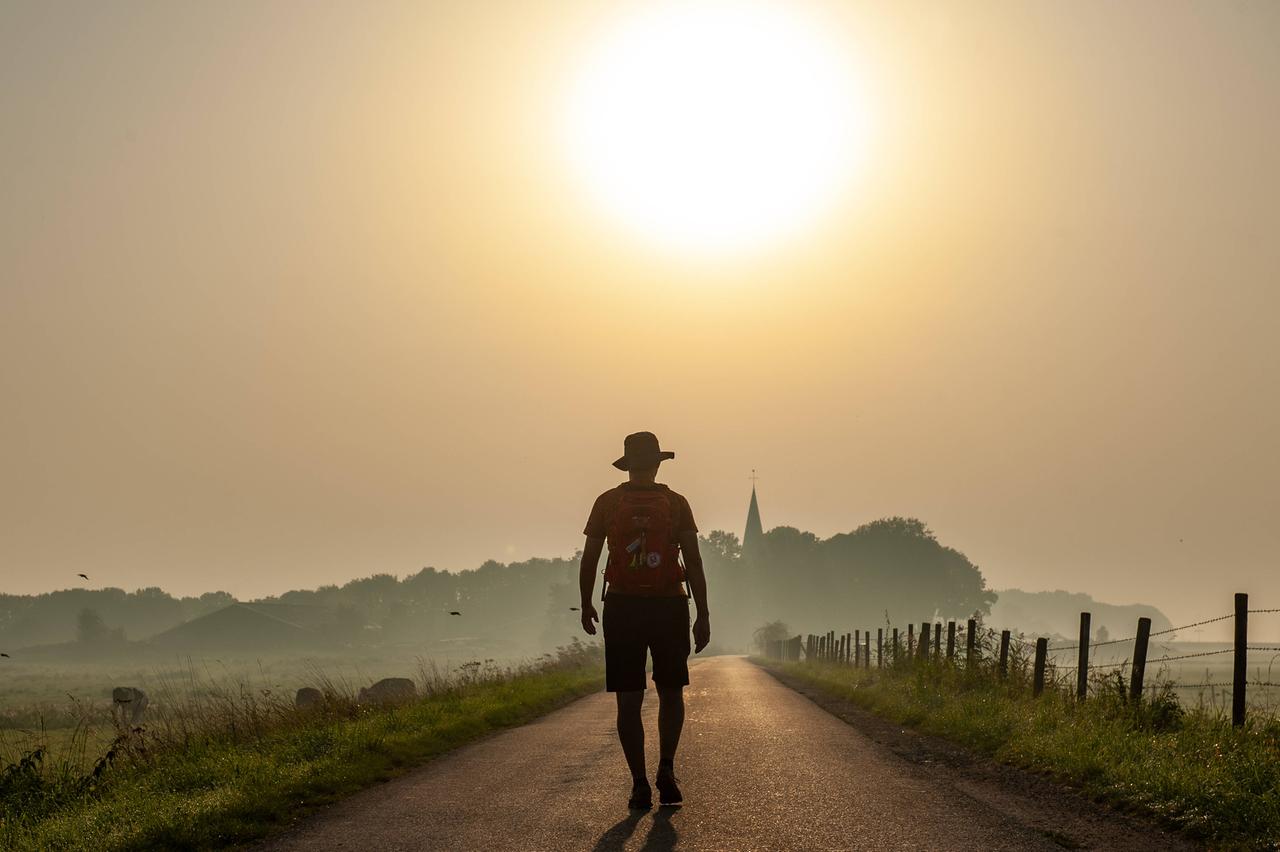 Ein Mann läuft während eines vernebelten Sonnenaufgangs auf einem Deich entlang. Das Bild symbolisiert die große Hitze, die der Klimawandel mit sich bringt.