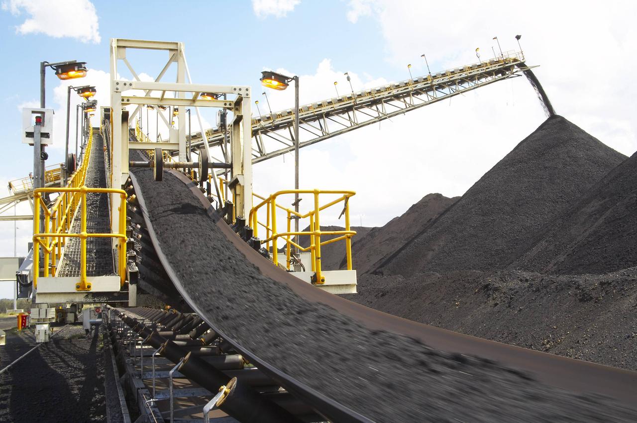 Ein Förderband transportiert Kohle in die Höhe, die auf einem großen schwarzen Berg abgeladen wird.