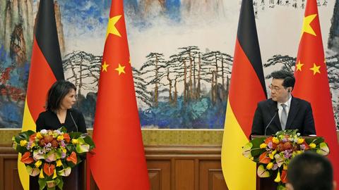 Annalena Baerbock, und Qin Gang R sprechen auf einer Pressekonferenz. Sie stehen an zwei Rednerpulten, hinter ihnen jeweils die Flaggen der beiden Länder.