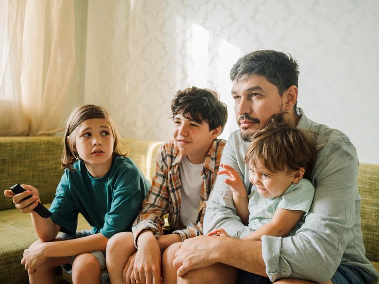 Ein Vater guckt mit seinen drei Kindern fern.