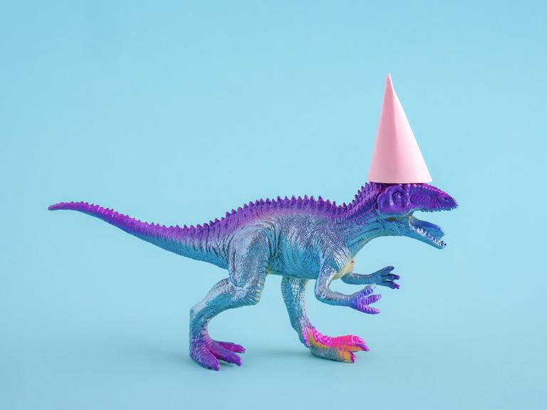 Süßer blau-lila-silbern glitzernder T-Rex mit einem pinken Partyhut auf blauem Hintergrund.