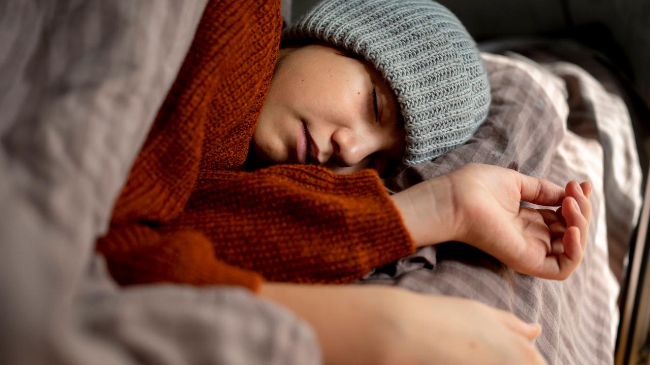 Ein Mensch mit Mütze schläft erschöpft in seinem Bett.