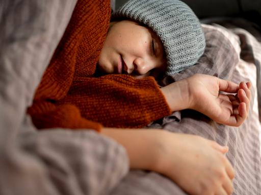 Ein Mensch mit Mütze schläft erschöpft in seinem Bett.