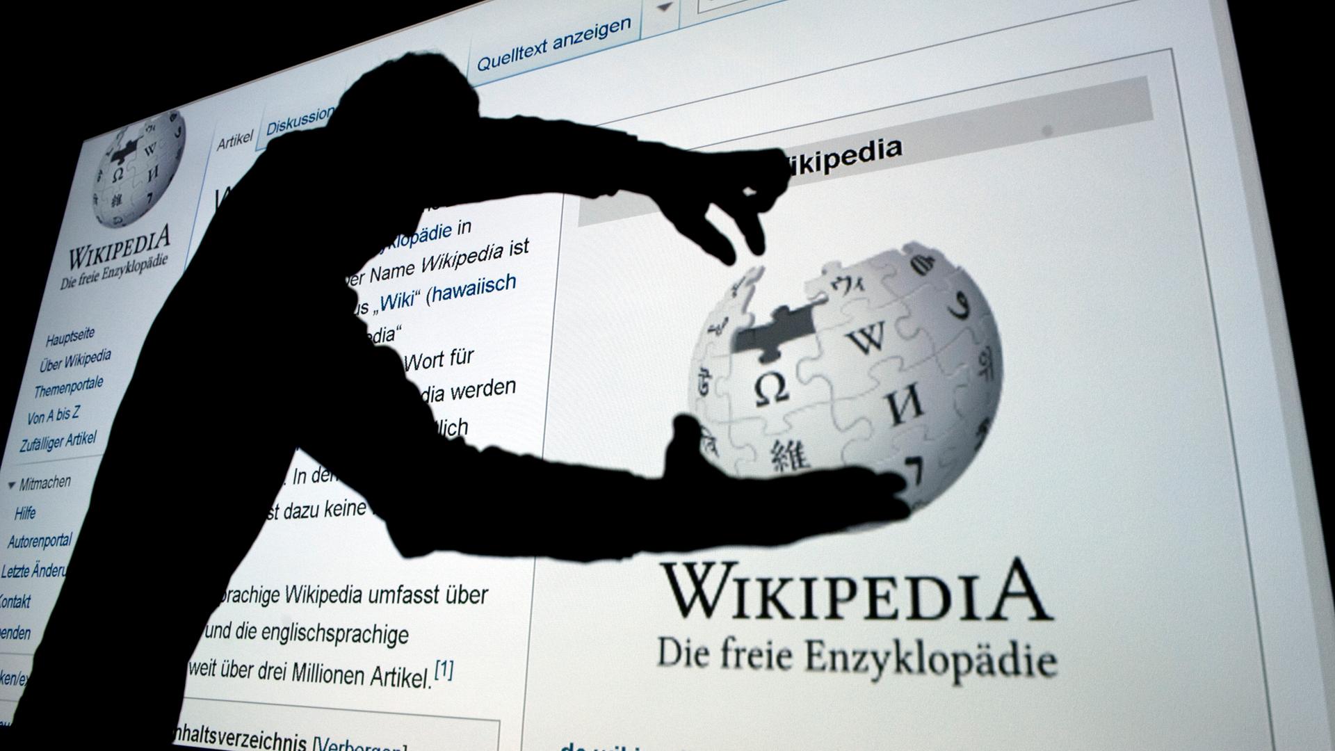 Der Schatten eines Mannes, der mit seinen Fingern nach einem dem Wikipedia-Globus greift.