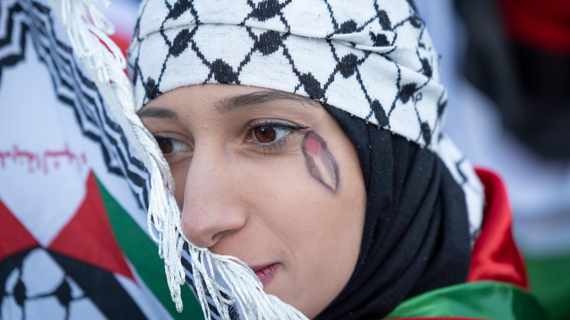 Eine Demonstrantin auf einer propalästinensichen Demo. Unter ihrem Auge ist eine Palästinenserflagge in Form einer Träne aufgemalt.