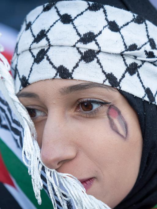 Eine Demonstrantin auf einer propalästinensichen Demo. Unter ihrem Auge ist eine Palästinenserflagge in Form einer Träne aufgemalt.