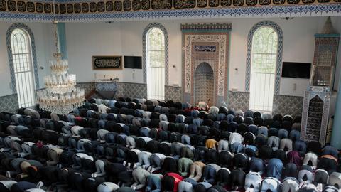 Muslime knieen mit dem Kopf auf dem Boden nebeneinander in einer Moschee.