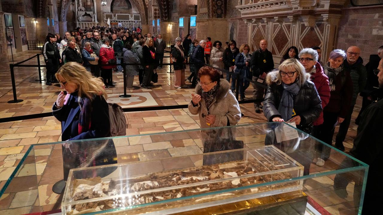Menschen stehen Schlange, um die gebeine des heiligen Franz von Assisi zu sehen, die in einem Glaskasten liegen
