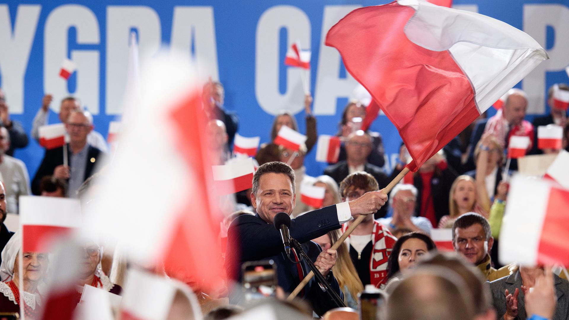 Rafał Trzaskowski schwenkt die polnische Flagge. Die Szene spielt sich am Sonntagabend, dem 18. Mai 2025, in Sandomierz ab. Im Hintergrund jubeln Unterstützer, viele halten kleine und große Polenfahnen in die Höhe. 