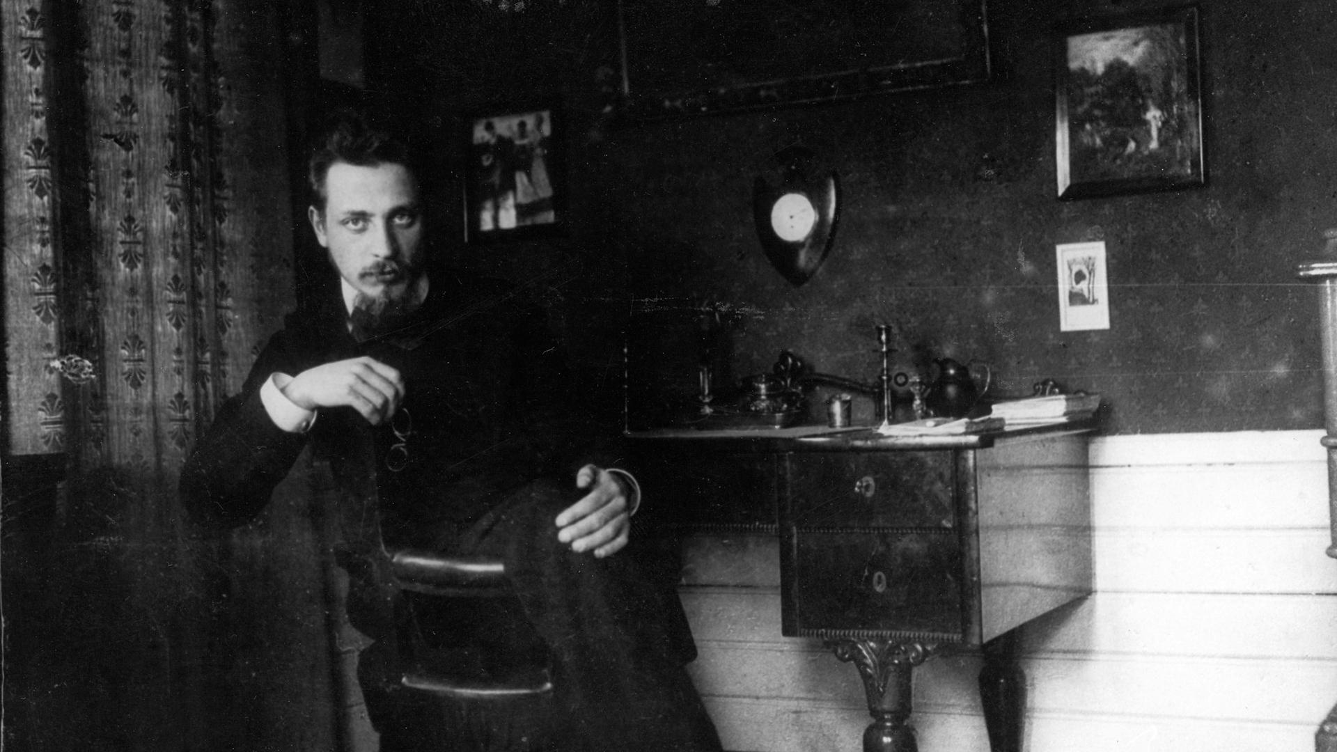 Der Dichter Rainer Maria Rilke sitzt um 1905 auf einem Stuhl in einem Zimmer.