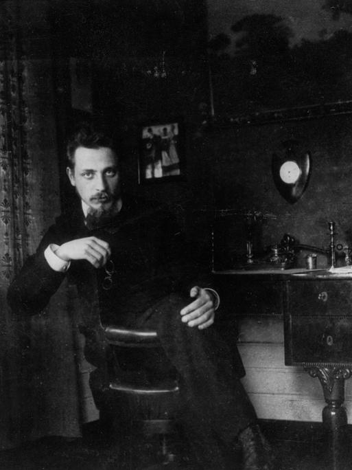 Der Dichter Rainer Maria Rilke sitzt um 1905 auf einem Stuhl in einem Zimmer.